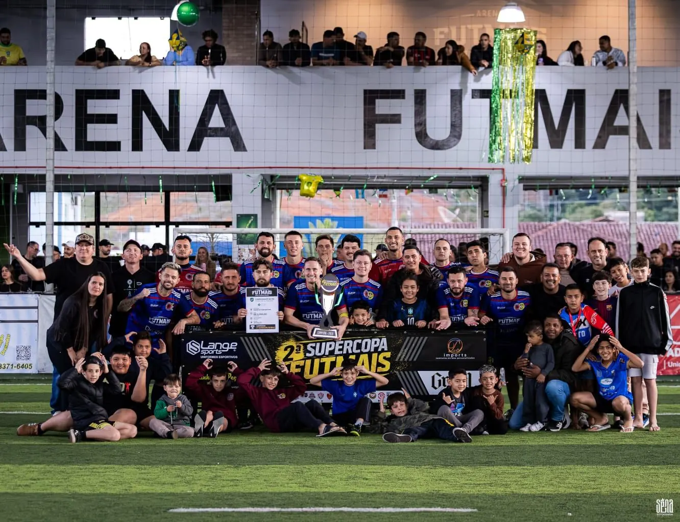 Time campeão da 2ª Supercopa Futmais com troféu, familiares e torcida na quadra