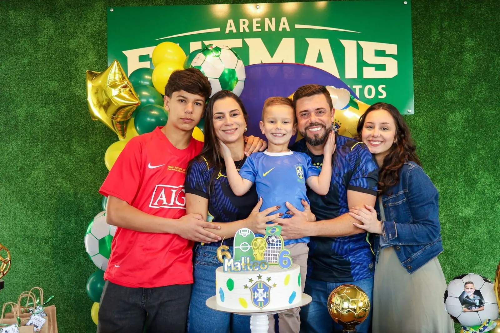 Família reunida em torno do bolo de aniversário, com decoração de futebol na Arena Futmais